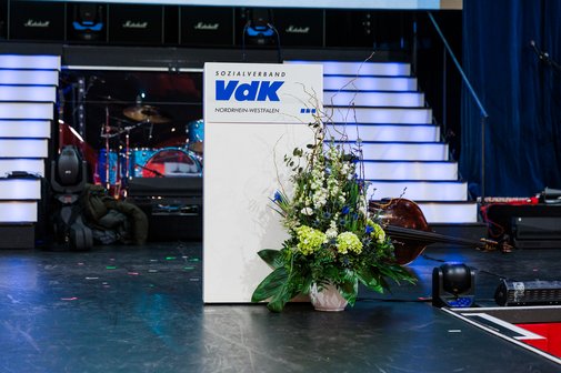 B&uuml;hne mit Rednerpult mit VdK-Logo und Blumenschmuck davor.