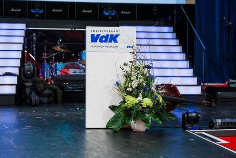 B&uuml;hne mit Rednerpult mit VdK-Logo und Blumenschmuck davor.
