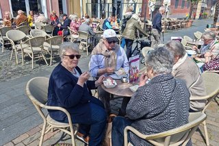 Eiscafé-Pause beim Stadtbummel: Menschen sitzen gemeinsam um Bistrotische herum und löffeln Eis.