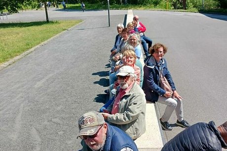 Eine Gruppe Menschen sitzt gemeinsam auf einer langen Mauer.