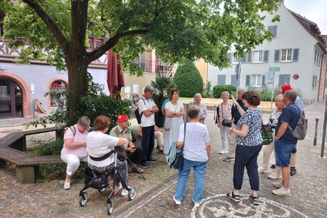 Bei einer Pause während der Stadtführung in Freiburg im Breisgau erzählt eine Stadtführerin aus der Geschichte der Stadt.