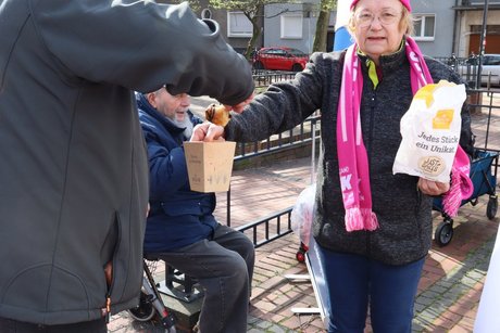 Eine Frau bietet einem Kollegen Geb&auml;ck an.