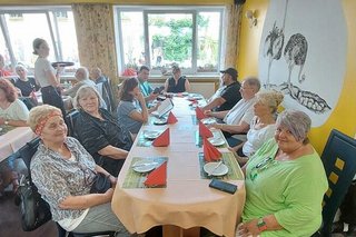 Menschen sitzen gemeinsam an Tischen im Restaurant der Straußenfarm. An der Wand gemalt sind Straußen.