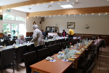 Vorstandsmitglieder treffen letzte Vorbereitungen in einem Raum mit mehreren langen Tischen, die gedeckt sind.