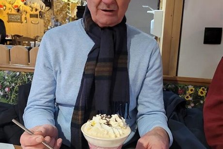 Ein Mann sitzt an einem Café-Tisch vor einer großen Tasse Rüdesheimer Kaffee mit Schlagsahne-Haube.