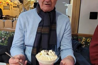 Ein Mann sitzt an einem Café-Tisch vor einer großen Tasse Rüdesheimer Kaffee mit Schlagsahne-Haube.