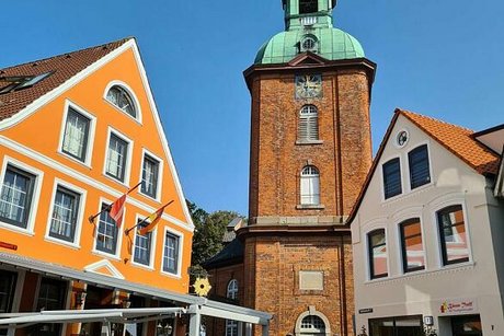 Blick auf den Kirchvorplatz in Kappeln mit gelbem Haus an der linken Seite und Kirchturm im Hintergrund.