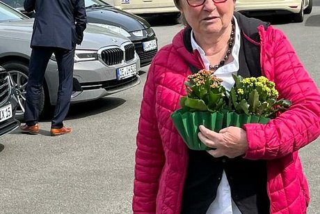 Hannelore Holterhof läuft mit Blumen auf dem Arm über den Parkplatz zu ihrem Auto