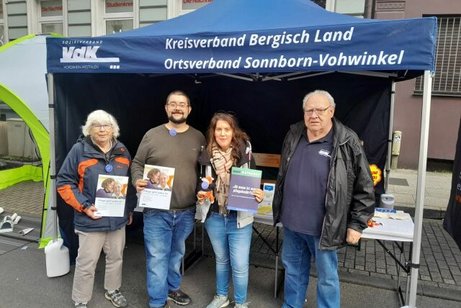 Zwei Frauen und zwei Männer stehen vor einem Pavillon des VdK Sonnborn-Vohwinkel und halten Broschüren in die Kamera.