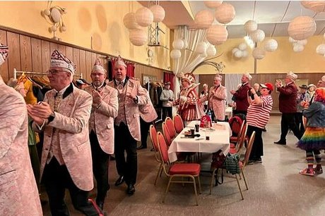 Menschen in Kostümen laufen klatschend hintereinander durch einen Saal.