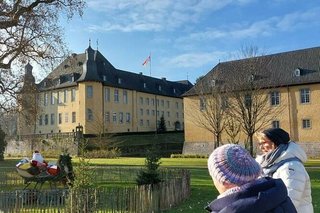 Zwei Frauen schauen auf einen Weihnachtsmann im Schlitten, der auf der Parkwiese der Burg als Dekoration aufgestellt wurde. Im Hintergrund sieht man das gelbe Schloss samt Nebengebäude.