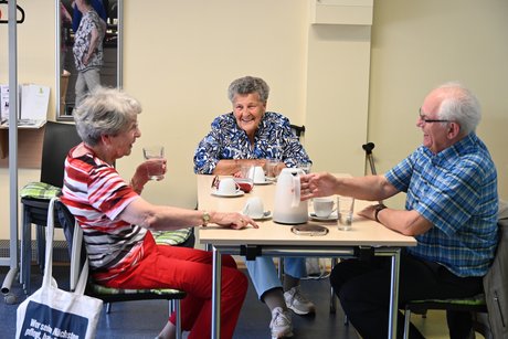 Menschen sitzen an Tischen bei Kaffee und Kuchen