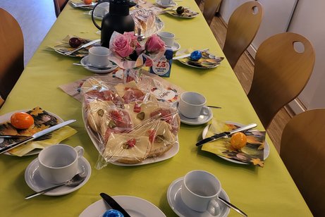 Ein Tisch mit grüner Decke, ein Tablett mit belegten Brötchen, eine Vase mit Rosa Rosen