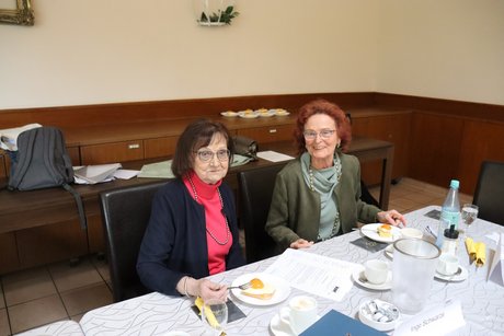Zwei Frauen sitzen an einem Tisch und schauen in die Kamera.