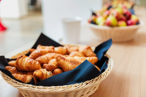 Im Vordergrund ein Korb mit kleinen Croissants, dahinter ein Obstkorb.