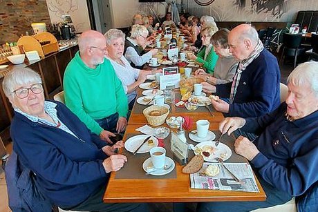 Viele Menschen sitzen gesellig beisammen an einer langen, reichlich gedeckten Frühstückstafel