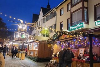 Lichterketten sind zwischen den Häusern über den Platz gespannt, auf dem sich Weihnachtsmarktbuden aneinanderreihen. Im Hintergrund leuchtet gut sichtbar die mehrstöckige Weihnachtspyramide.