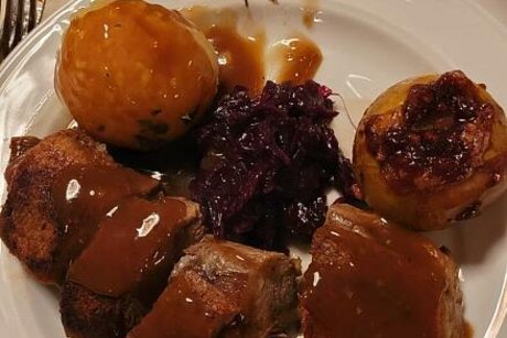Gänsebraten mit Rotkohl und Klößen liegen auf einem weißen Teller.