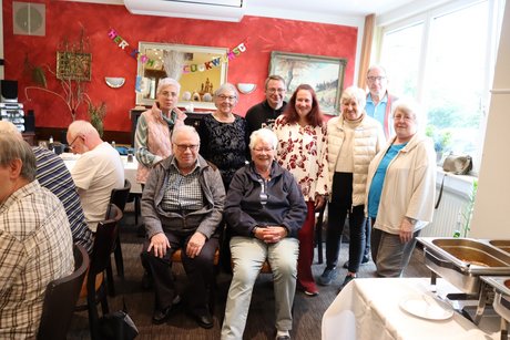 Mehrere Personen stehen oder sitzen f&uuml;r ein Gruppenbild zusammen.