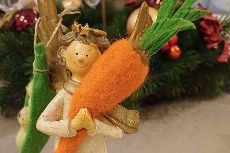 Ein Stoffengel h&auml;lt in den H&auml;nden eine M&ouml;hre aus Filz und tr&auml;gt auf einer Schulter Erbsen aus Filz.