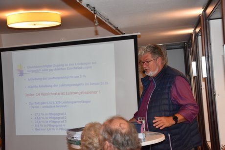 Klaus Meiers steht am Rednerpult und neben der Leinwand.