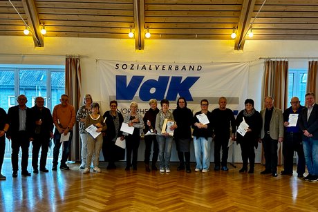 Menschen stehen mit Pr&auml;sent und Urkunde vor VdK Fahne