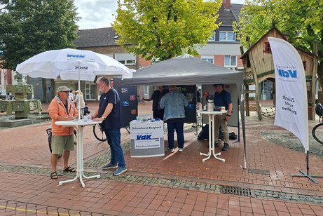 Marktstand in Borghorst, mit Sonnenschirm und Zeltpavillon. Am Stehtisch steht Herr Meiers und unterh&auml;lt sich mit einem Gast.