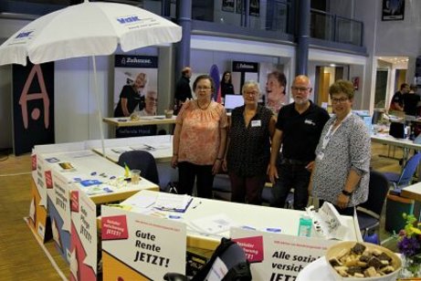 Drei Frauen und ein Mann stehen hinter Tischen mit Infomaterial. Links im Bild ein weißer Sonnenschirm mit VdK-Logo
