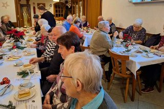 Menschen sitzen in einem Saal an Tischen bei Kaffee und Kuchen