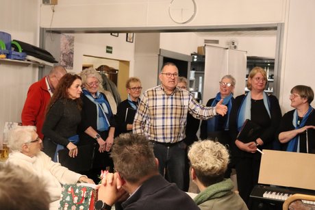 Ein Mann spricht zu einem Chor und den Teilnehmern.