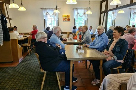 Menschen sitzen gemeinsam an Tischen in der Gaststube des Waffelhauses.