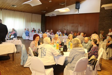 Mehrere Personen sitzen an runden Tischen und unterhalten sich miteinander.