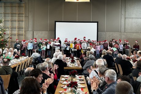 G&auml;ste an Tischen mit Kinderchor und Weihnachtsbaum im Hintergrund