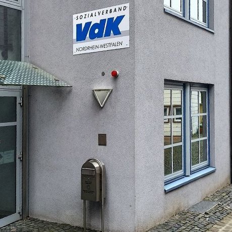 Glasüberdachter Eingang zur Kreisgeschäftsstelle mit weiß-blauem VdK-Logo an der Wand neben der Tür.