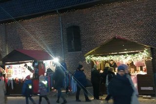 Menschen flanieren an beleuchteten Weihnachtsmarktbuden entlang, die vor den Mauern des Schlosses aufgebaut sind.