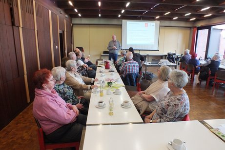 Ein Mann steht vor einer Leinwand und h&auml;lt einen Vortrag vor einer Gruppe.