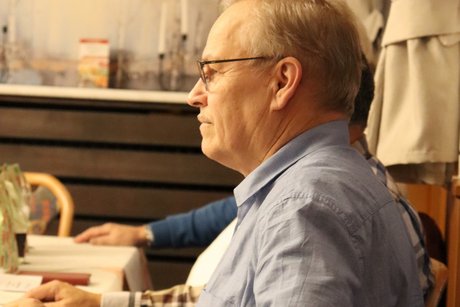 Ein Mann von der Seite fotografiert, h&ouml;rt jemandem zu.