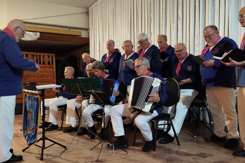 Chanty Chor Neuss Chanty Chor Neuss, 14 Männer und eine Frau mit weißen Hosen und blauen Oberteilen, teilweise sitzend und stehend. Die Sitzenden spielen verschiedene Instrumene