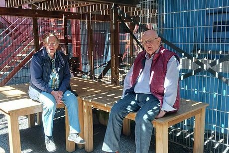 Zwei Männer sitzen im Schatten auf jeweils einem Tisch.