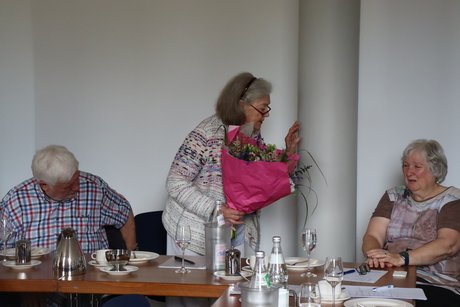 Jahreshauptversammlung 2026 Eine Frau mit einem Blumenstrauß in der Hand spricht mit einer sitzenden Frau.