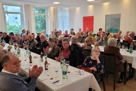 Viele Menschen sitzen an Tischen in einem Saal