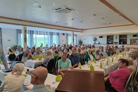 Viele Menschen sitzen an Tischen in einem Saal.