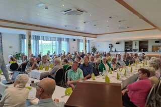 Viele Menschen sitzen an Tischen in einem Saal.