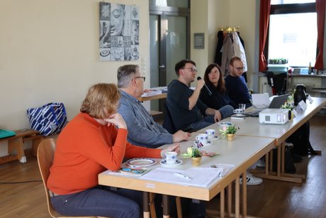 Treffen der Vertreterinnen der Frauen im Mehrgenerationenhaus. Fünf Personen sitzen an einem langen Tisch und ein Mann spricht zu den Anwesenden.