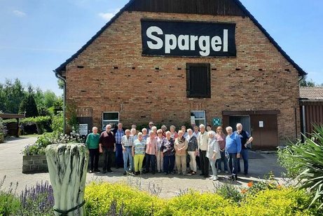 Gruppenfoto vor einer Scheune mit Aufschrift Spargel, im Vordergrund ein Blumenbeet
