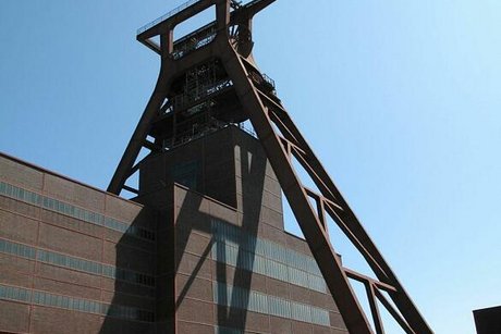 Oft als "Eiffelturm Essens" bezeichnet, hebt sich der markante, rostrote Förderturm der Zeche Zollverein vor strahlendblauem Himmel ab.