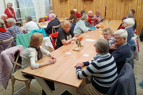 Man sieht M&auml;nner und Frauen an Tischen sitzen und sich unterhalten.
