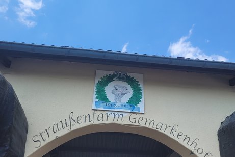 Man sieht einen Straussenkopf und einen runden Toreingang über dem Straussnfarm Gemarkenhof zu lesen ist