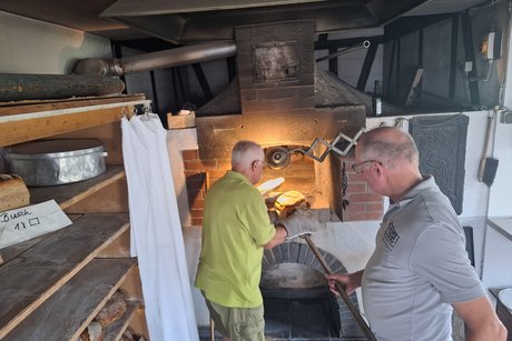 Mit zwei Mann werden die Brote zum Backen in die schmale Öffnung des Ofens geschoben.