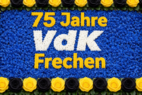 In der Art eines Maiherzens ist der Text "75 Jahre VdK Frechen" aus gelben und wei&szlig;en Bl&uuml;ten in eine Umgebung aus blauen Bl&uuml;ten gesteckt worden